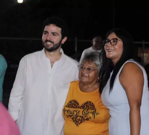Hombre con camisa blanca, mujer mayor con camiseta amarilla y mujer con vestido blanco posan sonriendo