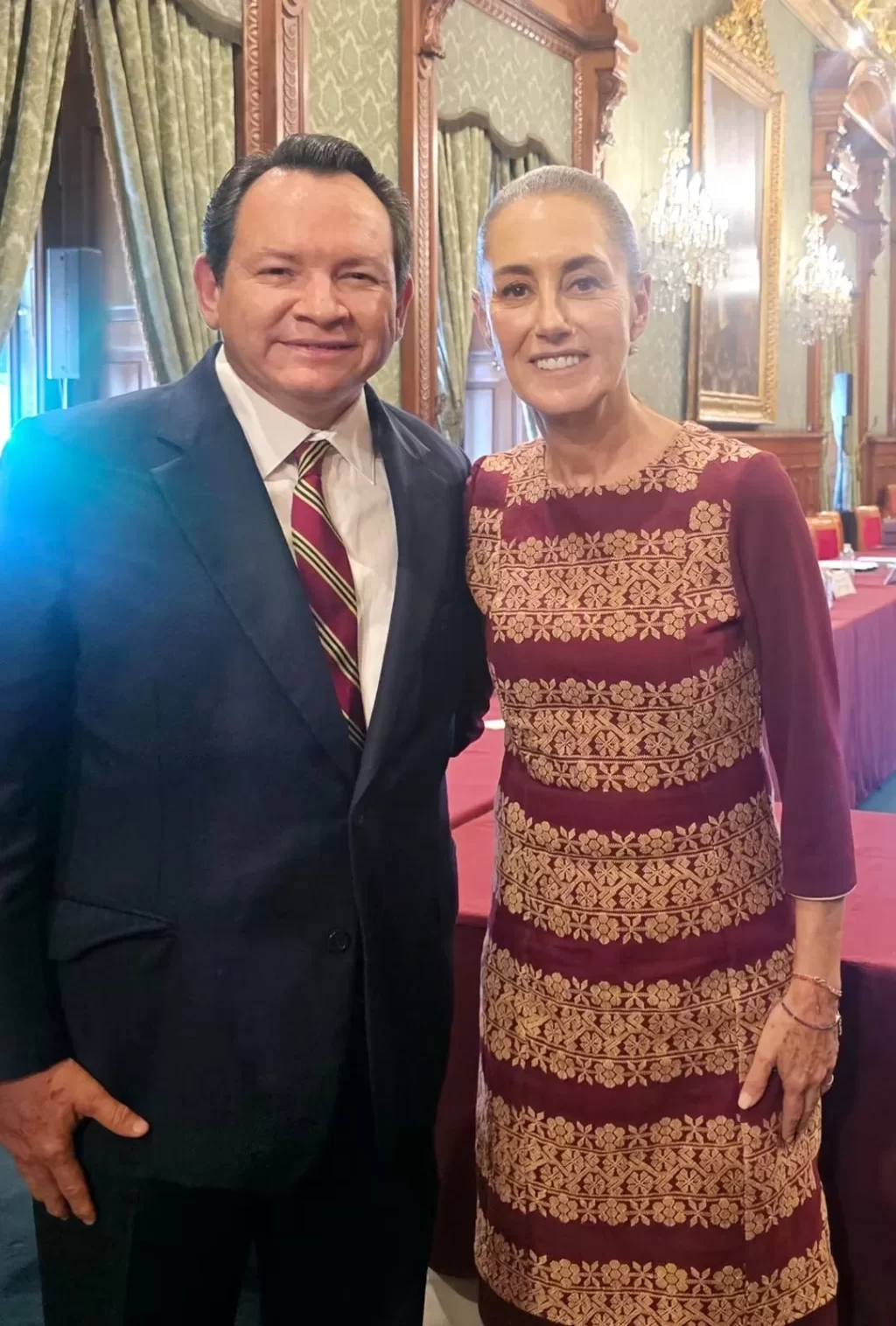 Hombre y mujer de pie juntos en salón con cortinas y candelabros al fondo
