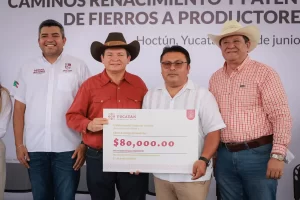 Cuatro hombres posando mientras uno sostiene un cheque simbólico de 80 mil pesos en Hoctún, Yucatán