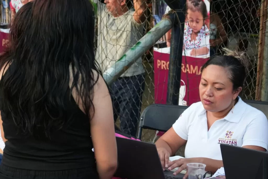 Mujer atendiendo a persona frente a computadora en un evento comunitario en Yucatán