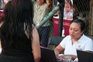 Mujer atendiendo a persona frente a computadora en un evento comunitario en Yucatán