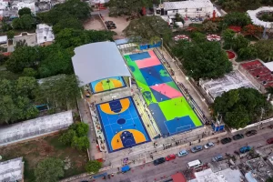 Vista aérea de cancha deportiva con áreas para baloncesto y fútbol, rodeada de árboles y edificaciones