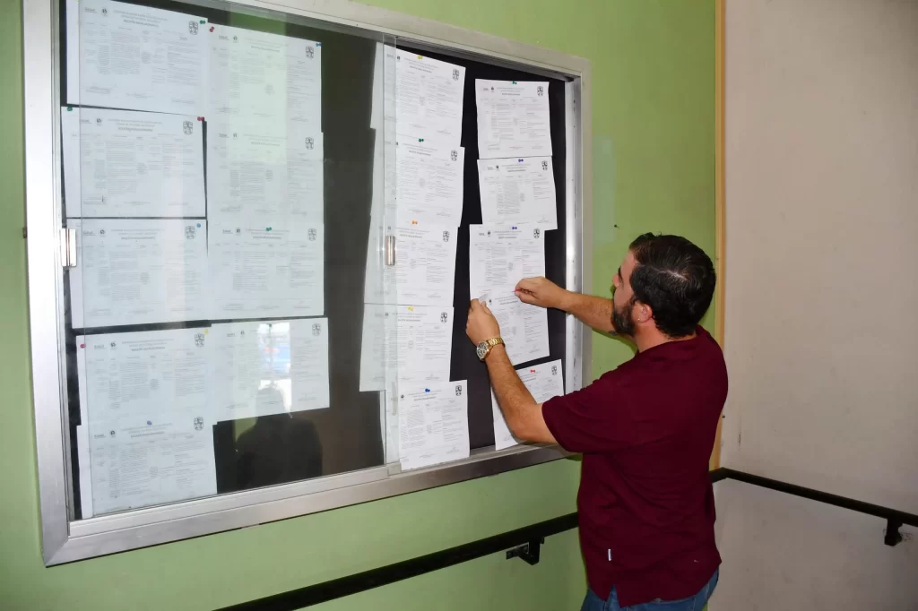 Hombre con camiseta vino coloca hoja en un tablero de información con varios documentos