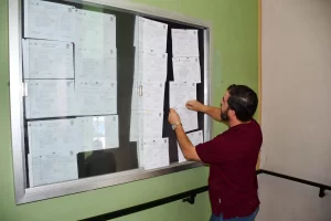 Hombre con camiseta vino coloca hoja en un tablero de información con varios documentos