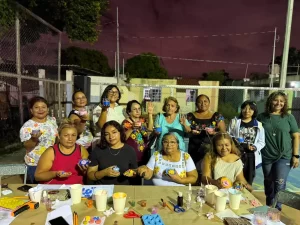Grupo de mujeres y niñas mostrando velas decoradas durante taller nocturno en cancha al aire libre