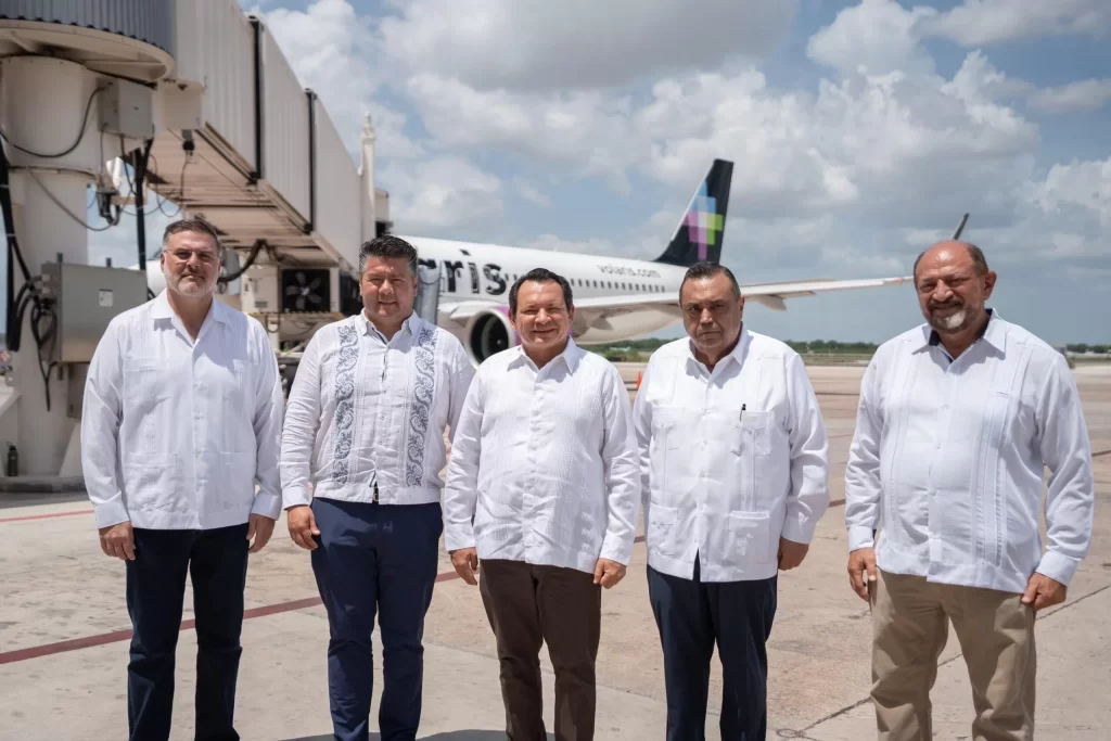 Cinco hombres con guayaberas blancas posando frente a avión de Volaris en la pista del aeropuerto
