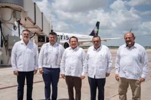 Cinco hombres con guayaberas blancas posando frente a avión de Volaris en la pista del aeropuerto