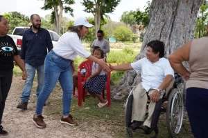 Mujer con gorra blanca saludando de mano a hombre en silla de ruedas bajo un árbol