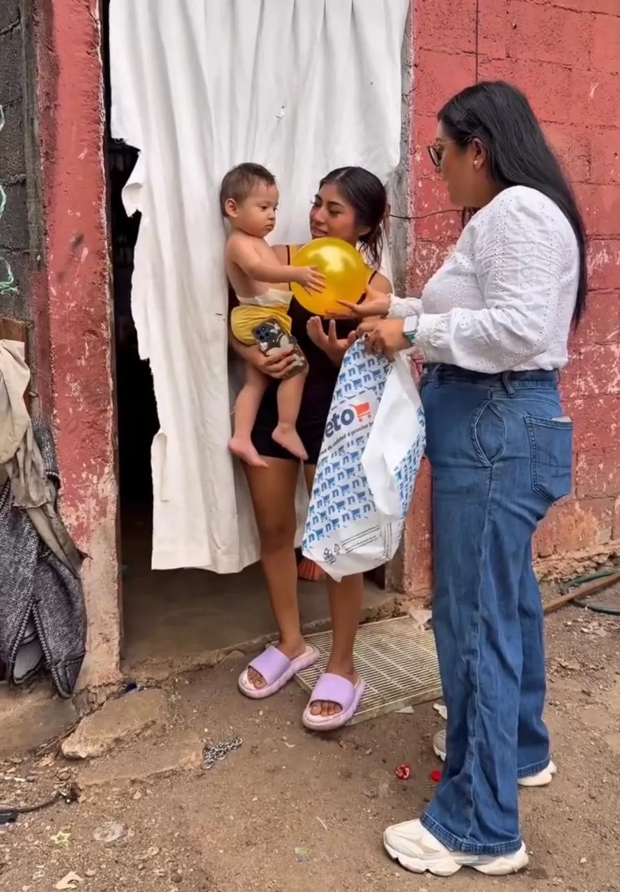 Mujer entrega un globo amarillo y bolsa de ayuda a madre con niño pequeño en casa