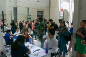 Varias personas en fila y sentadas en mesas realizando trámites o registros en un evento interior
