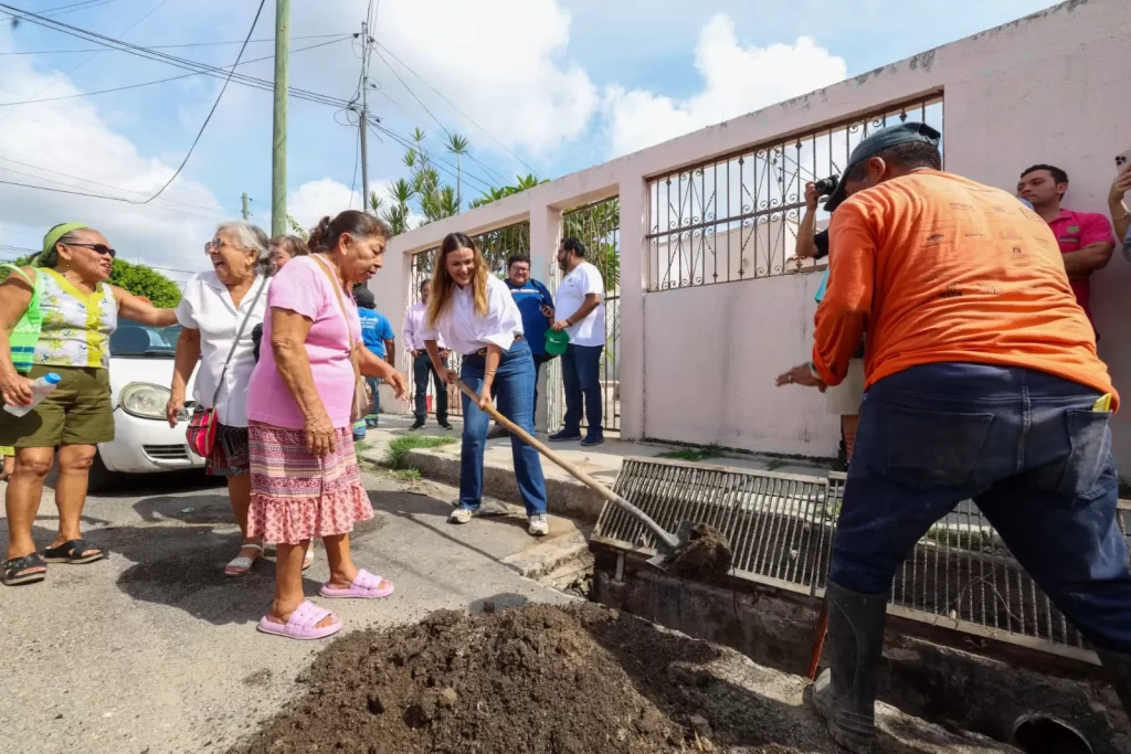 Personas adultas y una mujer joven limpiando una alcantarilla en la calle bajo un día soleado