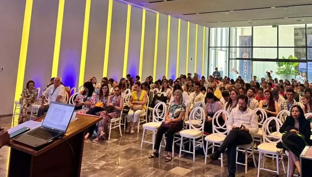Personas sentadas en sala con sillas blancas durante una conferencia o presentación