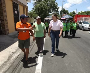 Grupo de personas caminando sobre calle pavimentada en día soleado, algunos con camisetas verdes y una mujer con blusa rosa y