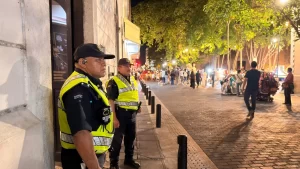 Dos policías con chalecos reflectantes al lado de edificio vigilando a personas en calle iluminada de noche