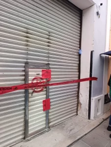 Persiana metálica con cinta roja de actividad suspendida y sellos oficiales