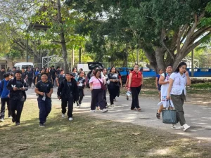 Grupo de estudiantes y profesores caminando por un camino rodeado de árboles y pasto bajo un día soleado