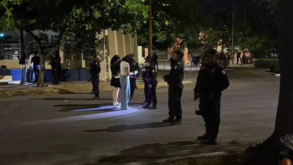Policías mexicanos revisan documentos a un grupo de personas en una calle iluminada por la noche