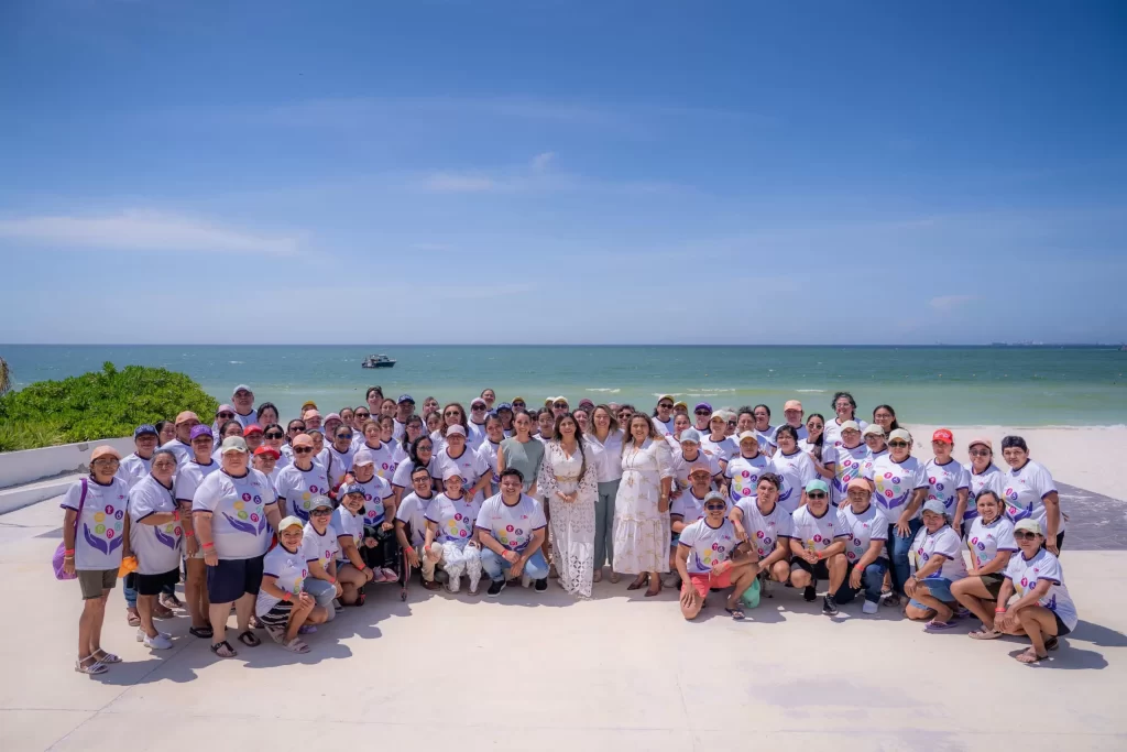 Gran grupo de personas posando en la playa frente al mar con camiseta blanca y gorras