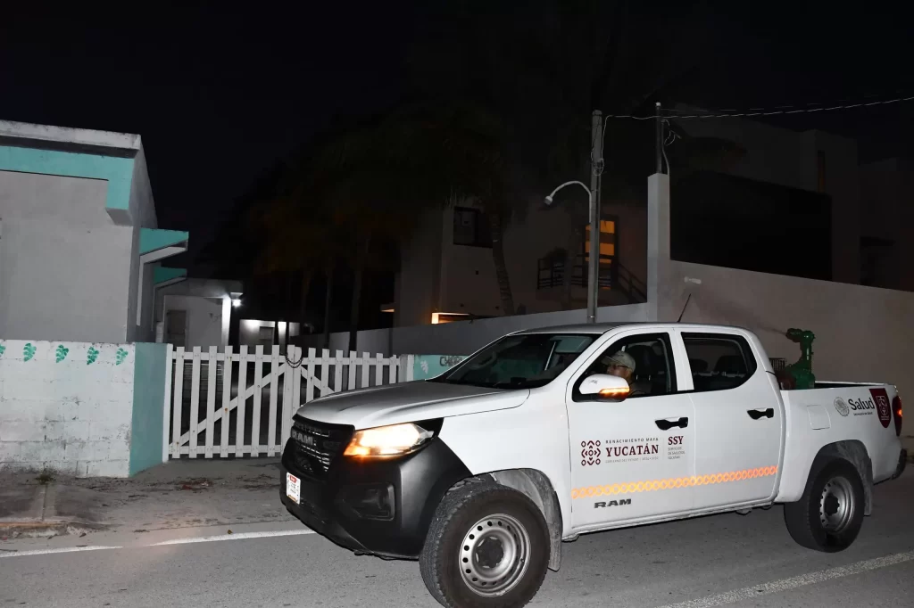 Camioneta blanca de Servicios de Salud de Yucatán circulando en calle residencial de noche