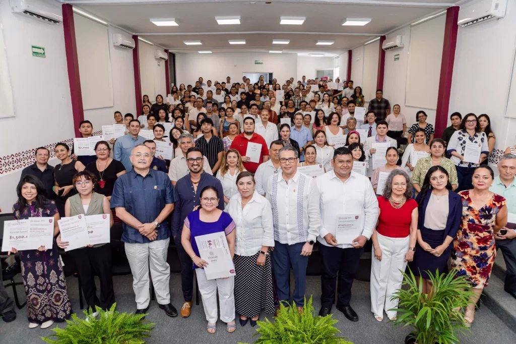 Grupo numeroso de personas posando en salón con reconocimientos y diplomas, ambiente formal