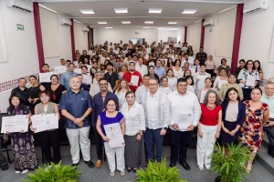 Grupo numeroso de personas posando en salón con reconocimientos y diplomas, ambiente formal