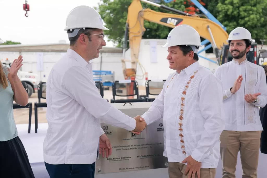 Dos hombres con casco blanco se dan la mano frente a placa conmemorativa en obra