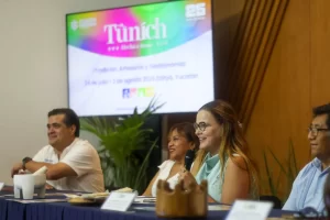 Personas en mesa de panel en evento Túnich con pantalla al fondo en Yucatán.