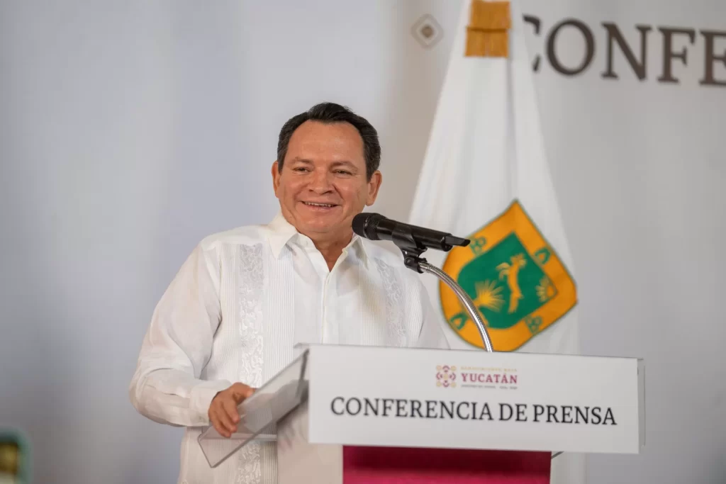 Hombre con guayabera blanca en conferencia de prensa en Yucatán sonriente frente a micrófono