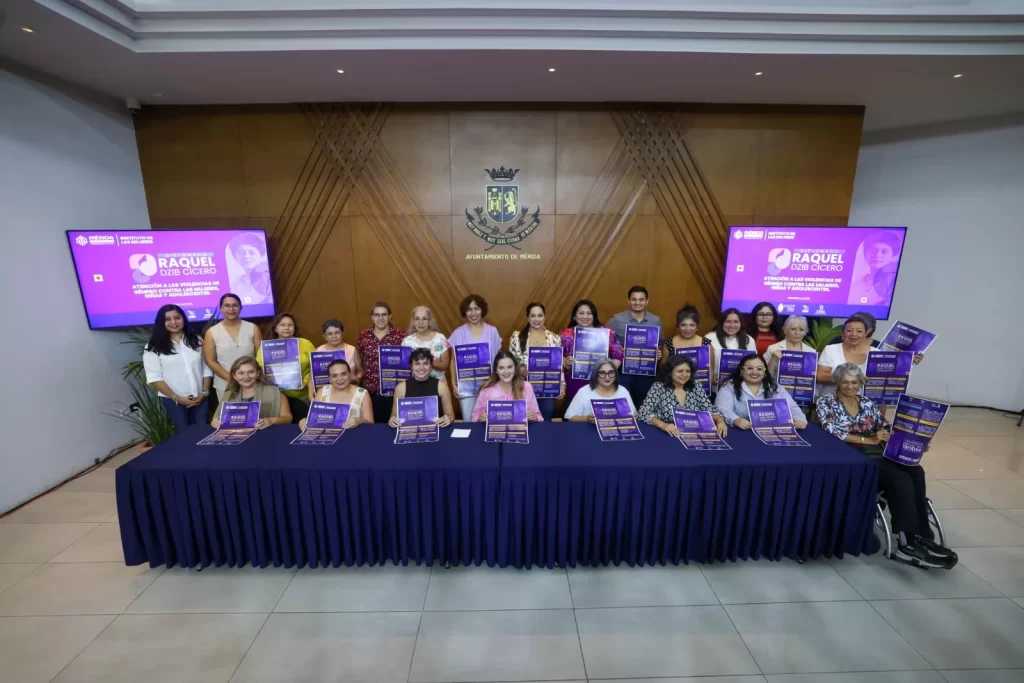 Grupo de personas posando con carteles morados en salón con escudo de Ayuntamiento de Mérida