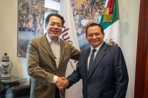 Dos hombres vestidos formalmente estrechándose la mano en oficina con bandera de México