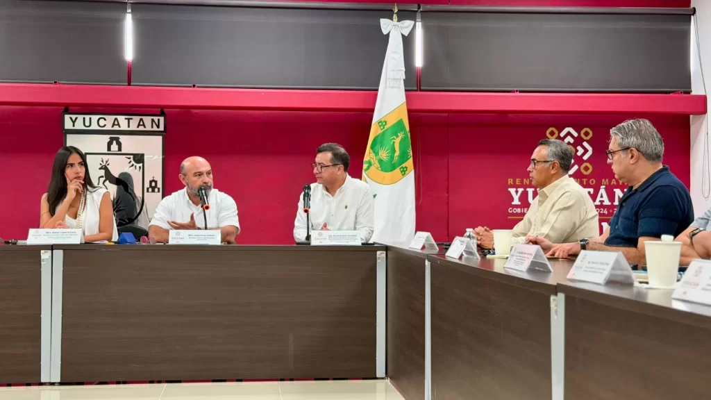 Personas en reunión oficial con banderas y escudo de Yucatán