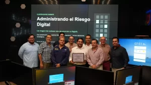 Grupo de diez hombres posando en una sala con pantallas donde se lee Administrando el Riesgo Digital
