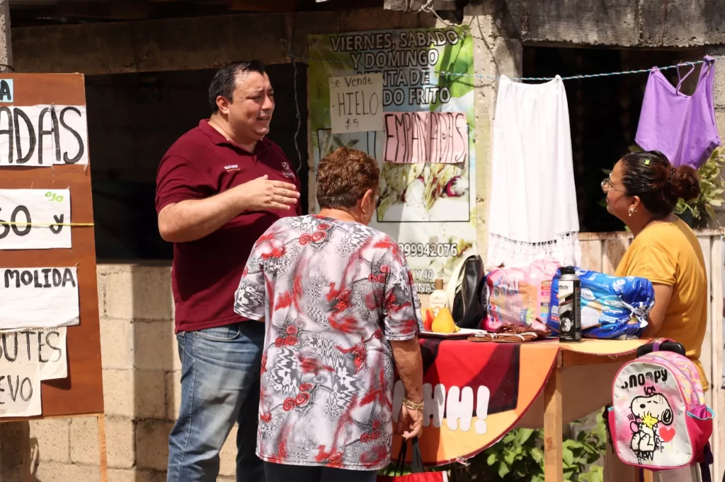 Tres personas en puesto callejero con anuncios de venta de empanadas y hielo
