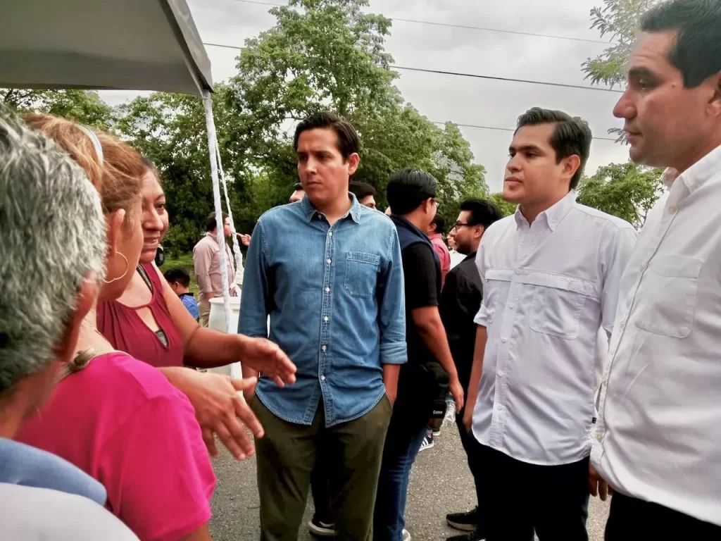 Grupo de personas conversando en un espacio al aire libre con árboles y cielo nublado al fondo