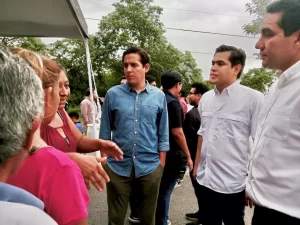 Grupo de personas conversando en un espacio al aire libre con árboles y cielo nublado al fondo